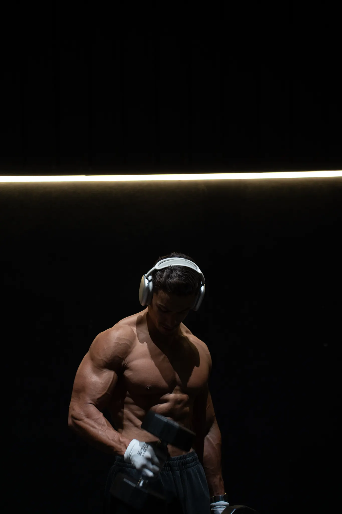 Rayan traint alleen met een dumbbell in een donkere sportschool